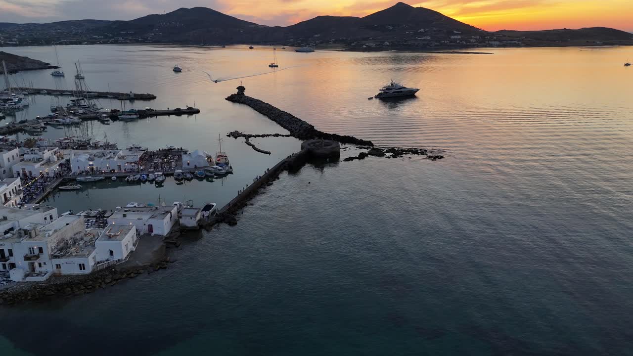 Paros Island,Aerial birds eye view,pan right from Naoussa town towards ancient Venetian castle's tower at harbor to the sunken sun behind the hills.Beautiful scenery with colorful sky