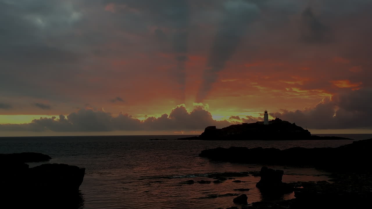 광선이 노란색, 주황색, 빨간색, 와이드 샷으로 빛나는 godrevy 등대의 극적인 불 같은 바다