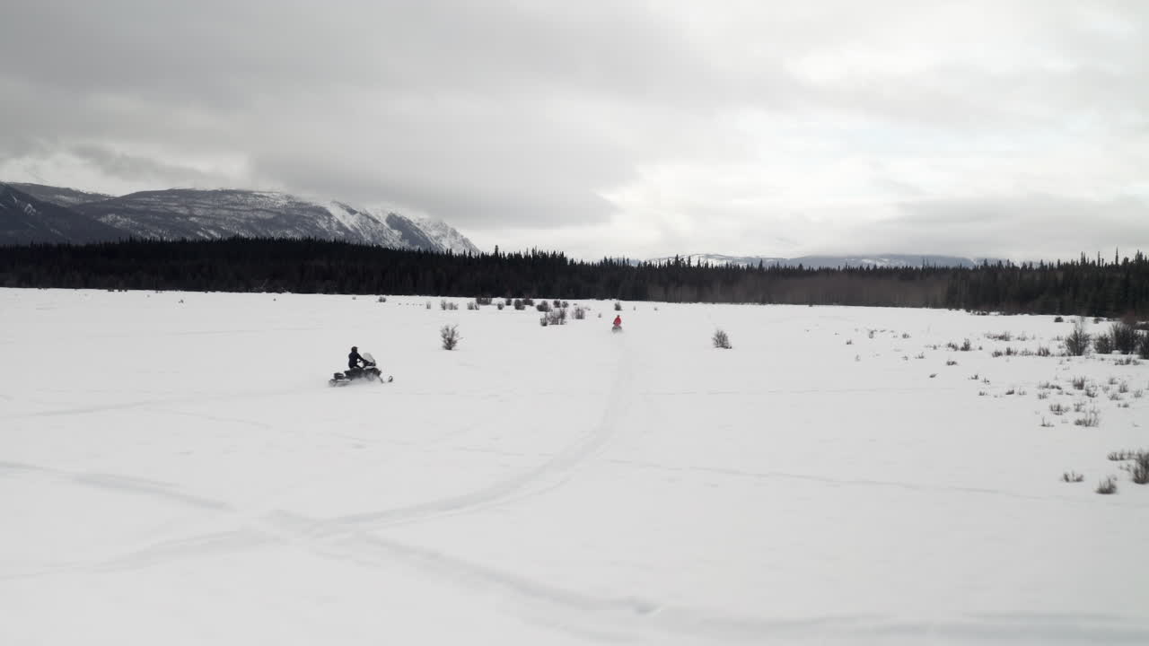 Ripresa con drone di due persone in motoslitta su un campo innevato.