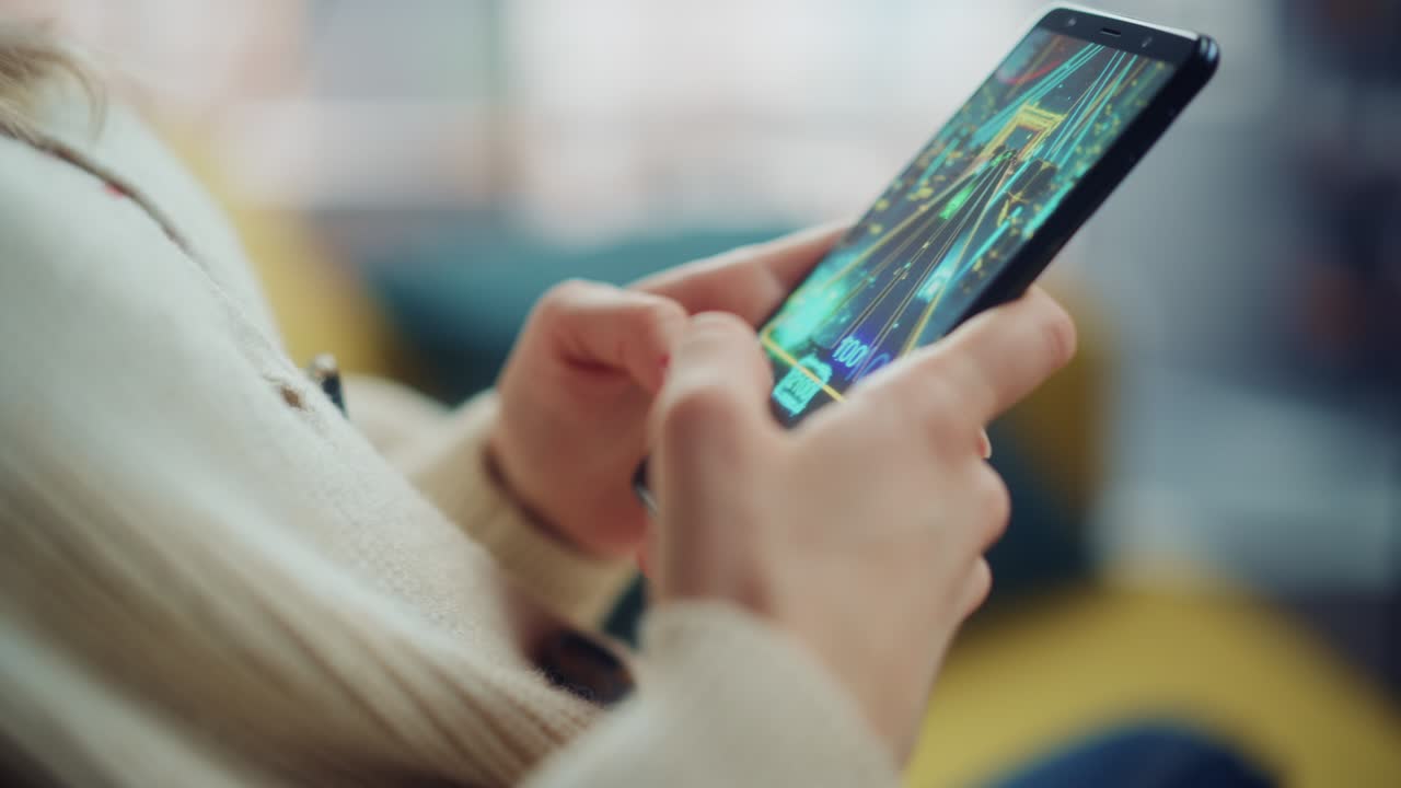 cerca de las manos de una persona jugando un videojuego de arcade en un teléfono inteligente sostenido verticalmente en la sala de estar de la casa. manos femeninas tocando la pantalla del teléfono móvil con un juego colorido a través de internet.