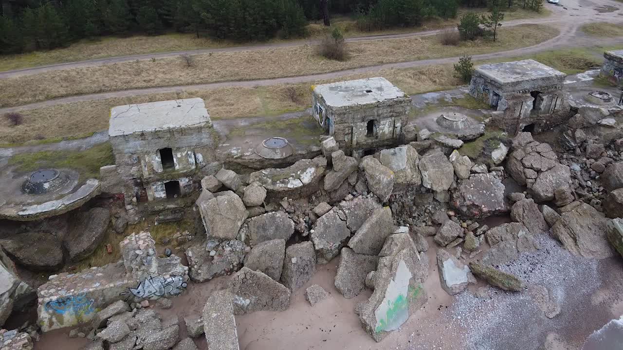 Aerial view of abandoned seaside fortification building at Karosta Northern Forts on the beach of Baltic sea in Liepaja in overcast spring day, pine wood, wide revealing drone shot moving backwards