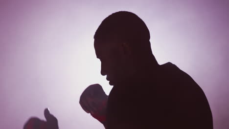 Dramatic-Backlit-Shot-Of-Male-Boxer-In-Gym-Wearing-Wraps-On-Hands-Training