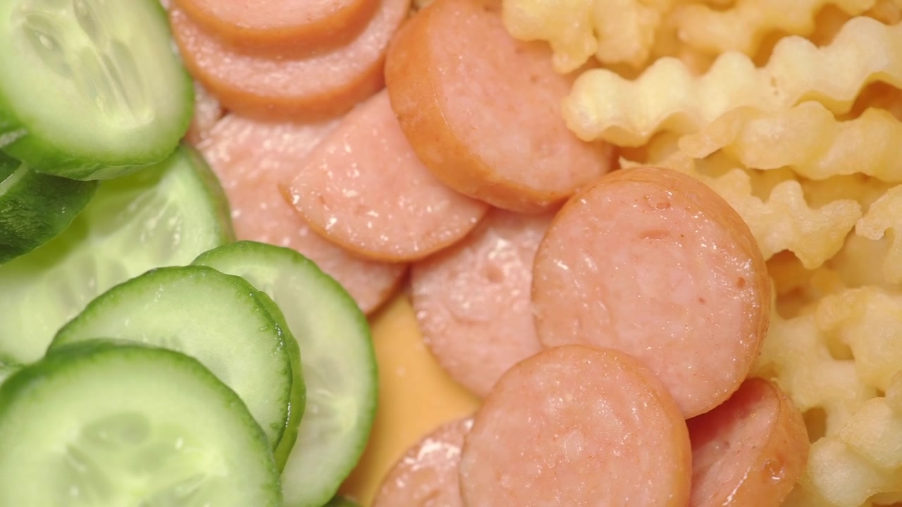 Nærbillede af skåret pølse, bølgeskårne pommes frites og agurk