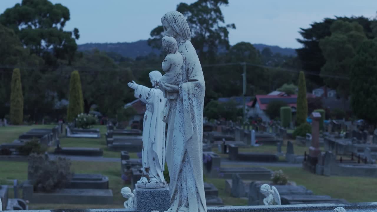 Pemandangan kuburan yang tenang di Ferntree Gully, Melbourne, menampilkan patung-patung khidmat saat matahari terbenam. Suasana damai, komposisi seimbang, dan pencahayaan lembut menciptakan nuansa reflektif.