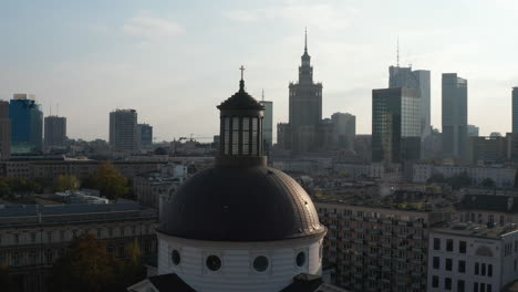 Fly-around-dome-of-Holy-Trinity-Church-with-golden-cross-on-top.-Cityscape-with-high-rise-buildings-in-background.-Warsaw,-Poland