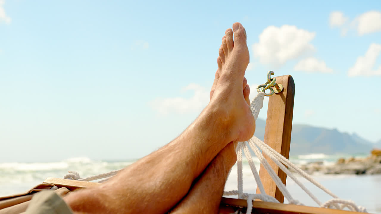 Primo piano del piede di un uomo appoggiato su un'amaca in spiaggia 4k
