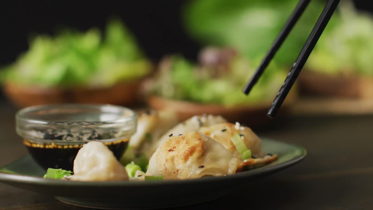 Chopsticks with gyoza dumpling on plate over vegetables on black background