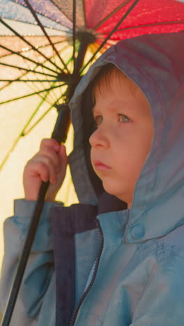 boy holds umbrella as rainfall persists. thoughtful child finds in uncomfortable place with emotions mirroring turbulence of weather. distress in solitude