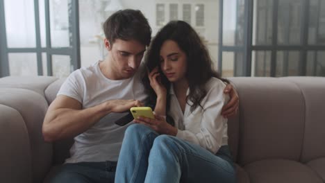 happy couple sitting on sofa with mobile phones together. smiling man and woman