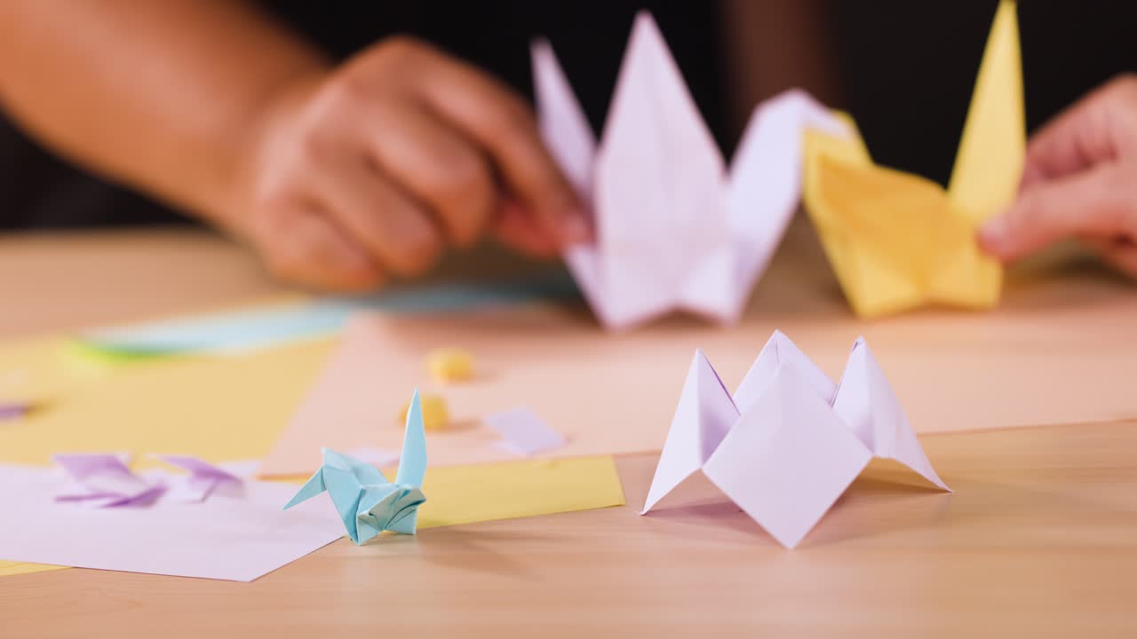Primo piano di mani che posizionano con cura diverse gru origami di carta piegata su un tavolo luminoso
