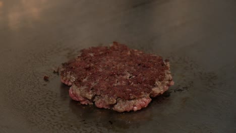 chef flipping burger patty with spatula in hot cooking stove, close up shot