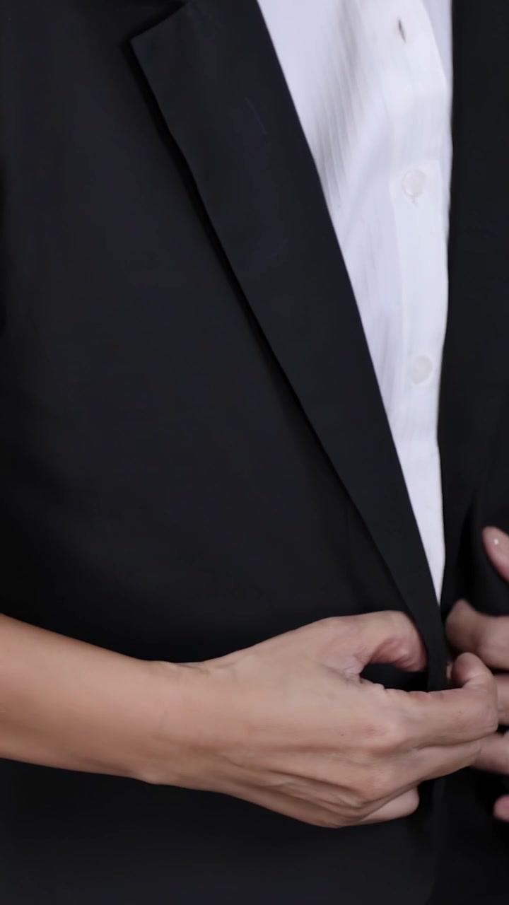 Primo piano di una donna in abbigliamento formale che si sistema la giacca del tailleur e la camicia bianca.