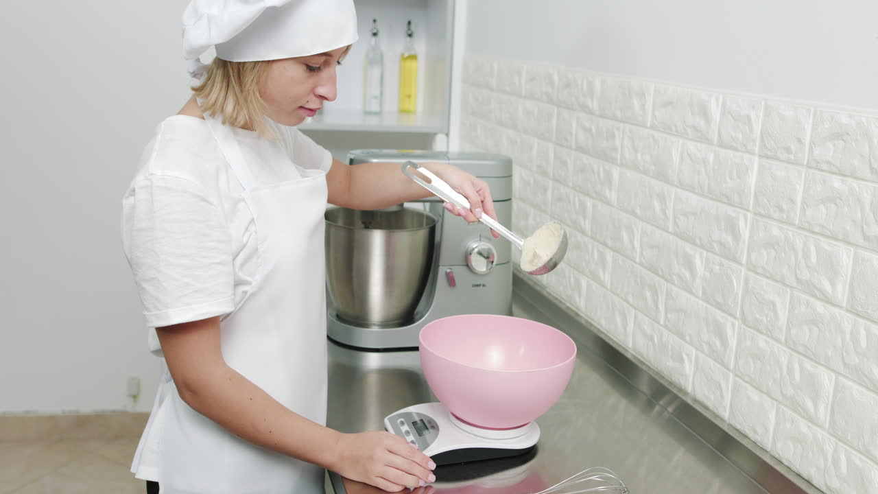 Primo piano dal basso di una giovane e attraente chef che aggiunge la farina in una ciotola rosa su una bilancia elettronica