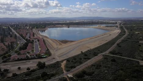 An-upward-pan-left-aerial-view-of-the-upper-San-Gabriel-reservoir-at-the-foothiils-of-the-mountians,-surrounded-by-single-family-homes-and-industrial-development-out-into-the-distance