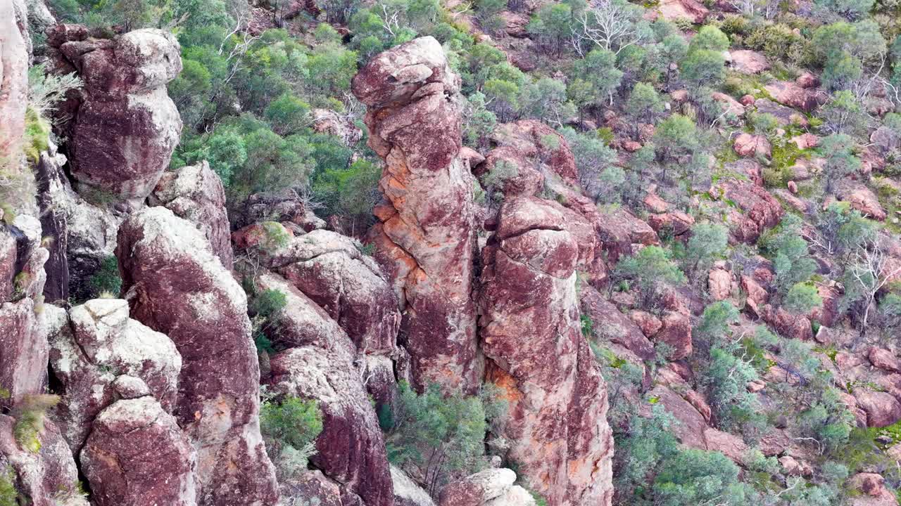 Drone glides above rugged sandstone pillars and bushland in soft, natural daylight, wide aerial view