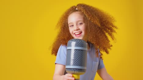 studio shot of girl singing karaoke into toy inflatable microphone against yellow background - shot in slow motion