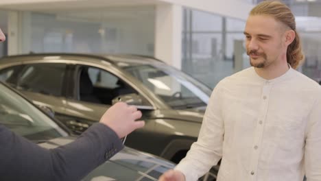 male hand gives a car keys to male hand in the car dealership close up. dealer giving key to new owner in auto show or salon.