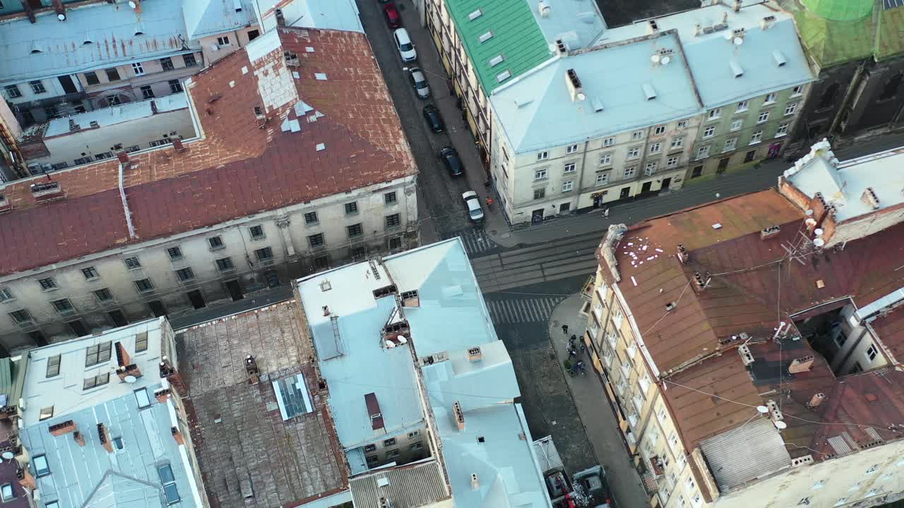Vista aérea de edifícios europeus e pessoas caminhando pelas ruas de Lviv, Ucrânia, com carros estacionados na estrada.