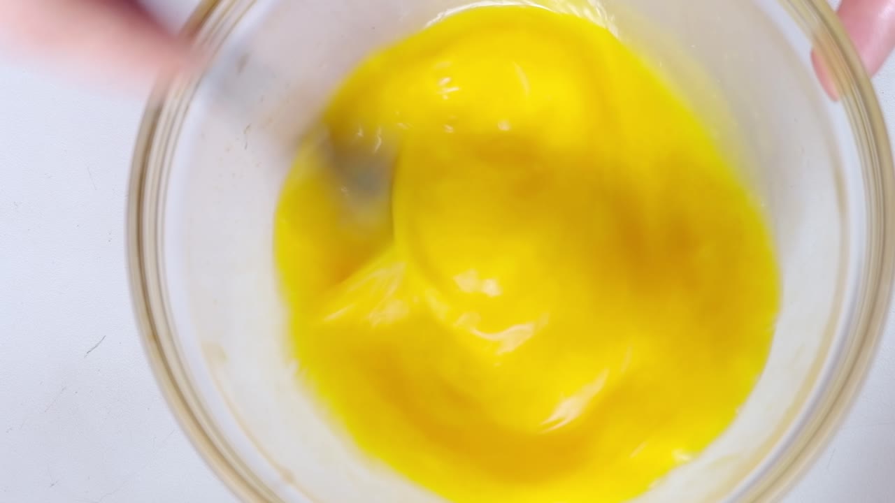 Woman beating eggs with a fork in a glass bowl