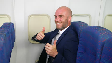 Close-up-of-a-happy-attractive-man-on-airliner-plane-giving-two-thumbs-up-and-smiling-flying-as-a-passenger-on-vacation