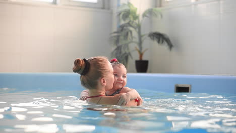 beautiful mother teaching cute baby girl how to swim in a swimming pool. child having fun in water with mom.