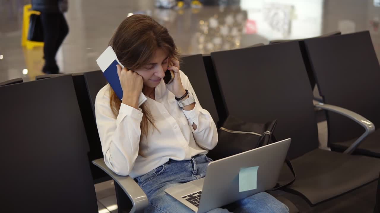 chica elegante y bonita con camisa blanca utiliza el teléfono y la computadora portátil para trabajar en el aeropuerto mientras espera el embarque en la sala de salida. hablando