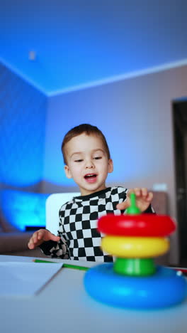 adorable caucasian child building pyramid on the desk. cute child learning colors and sizes at home. vertical video.
