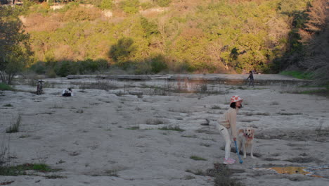 Perro-Asiático-Femenino-Lanzando-Una-Pelota-En-Un-Lecho-De-Río-Vacío-Al-Atardecer