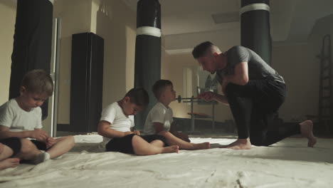 trainer scolds bad student in martial arts club. little children listen to professional instructor sitting on floor in gym slow motion. combat lesson