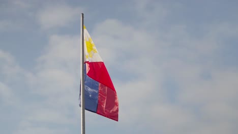 bandera filipina revoloteando en el viento en un asta de bandera contra un cielo azul ligeramente nublado