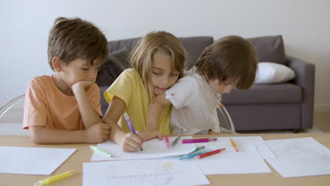 Pensive-girl-painting-with-markers-and-talking-with-brothers