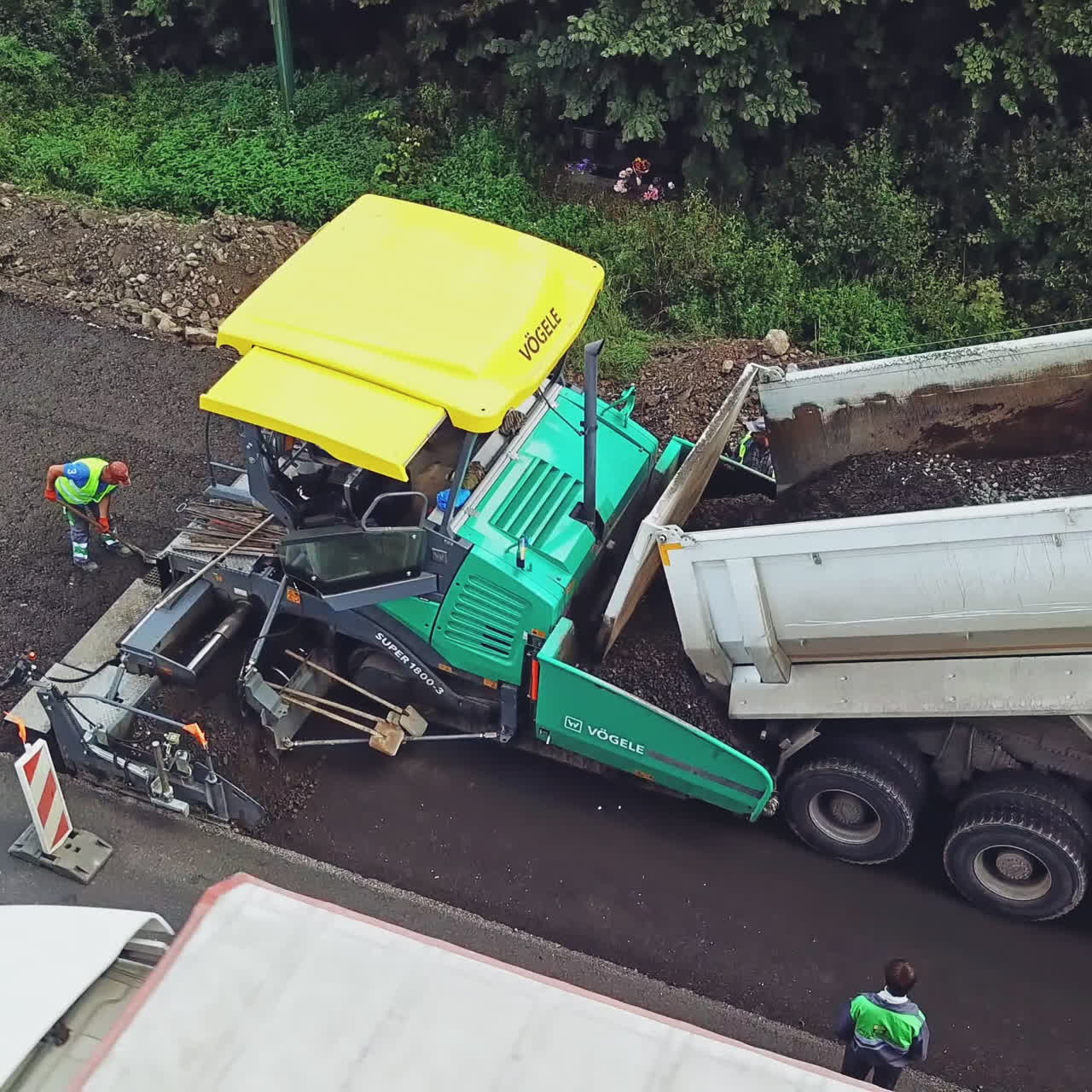 Heavy truck is pouring out new asphalt into the construction machinery. Roadworks repaving process on the background of black road. Aerial view.
