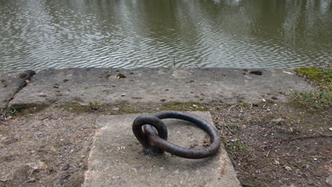 close up of a canal boat mooring ring on a dock next to the river