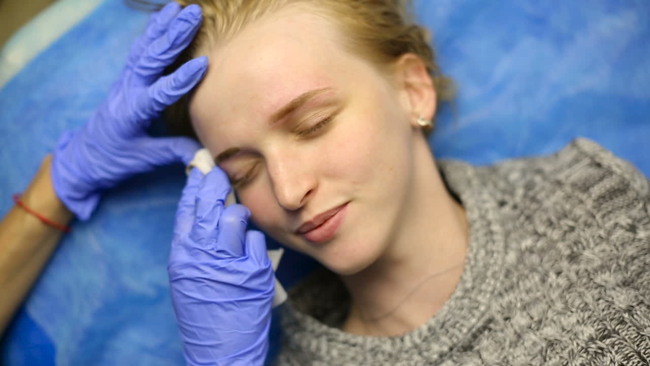 Woman in process of eyebrow tattoo. Close up of cosmetologist making permanent makeup