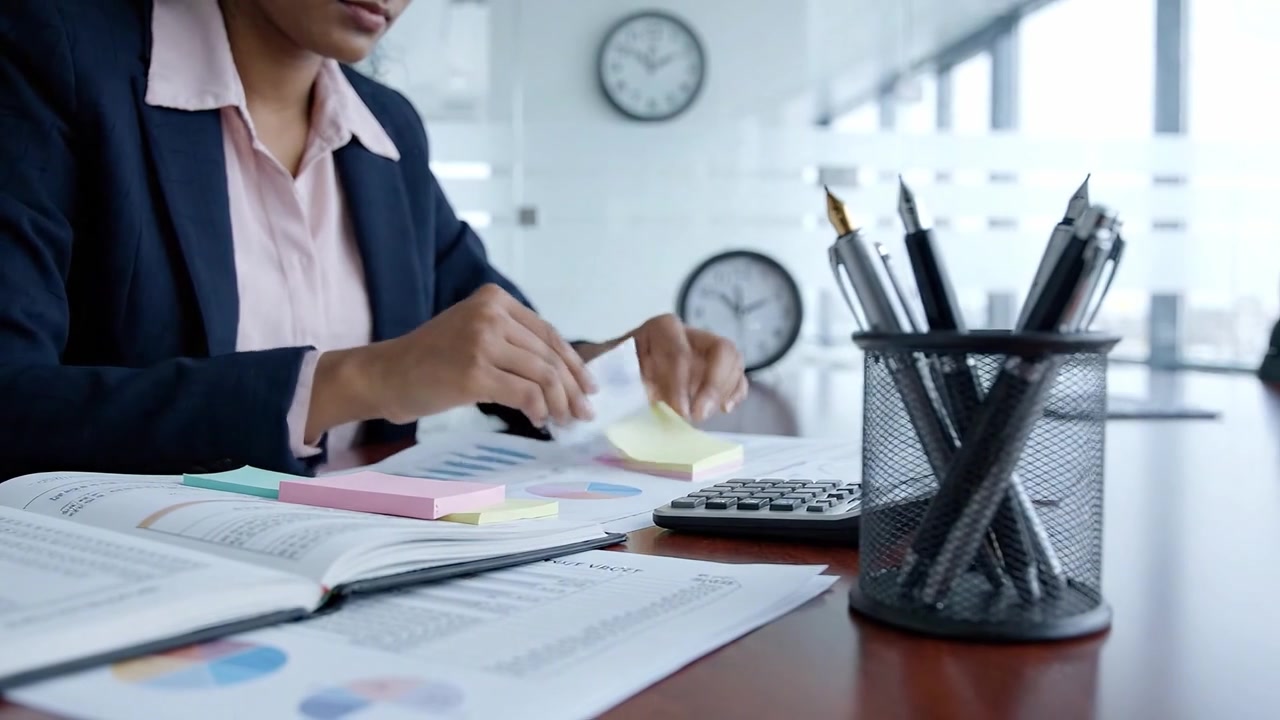 Profesional concentrado analizando datos con notas adhesivas, gráficos y una calculadora en un entorno de oficina moderno, mostrando dedicación a una planificación financiera meticulosa