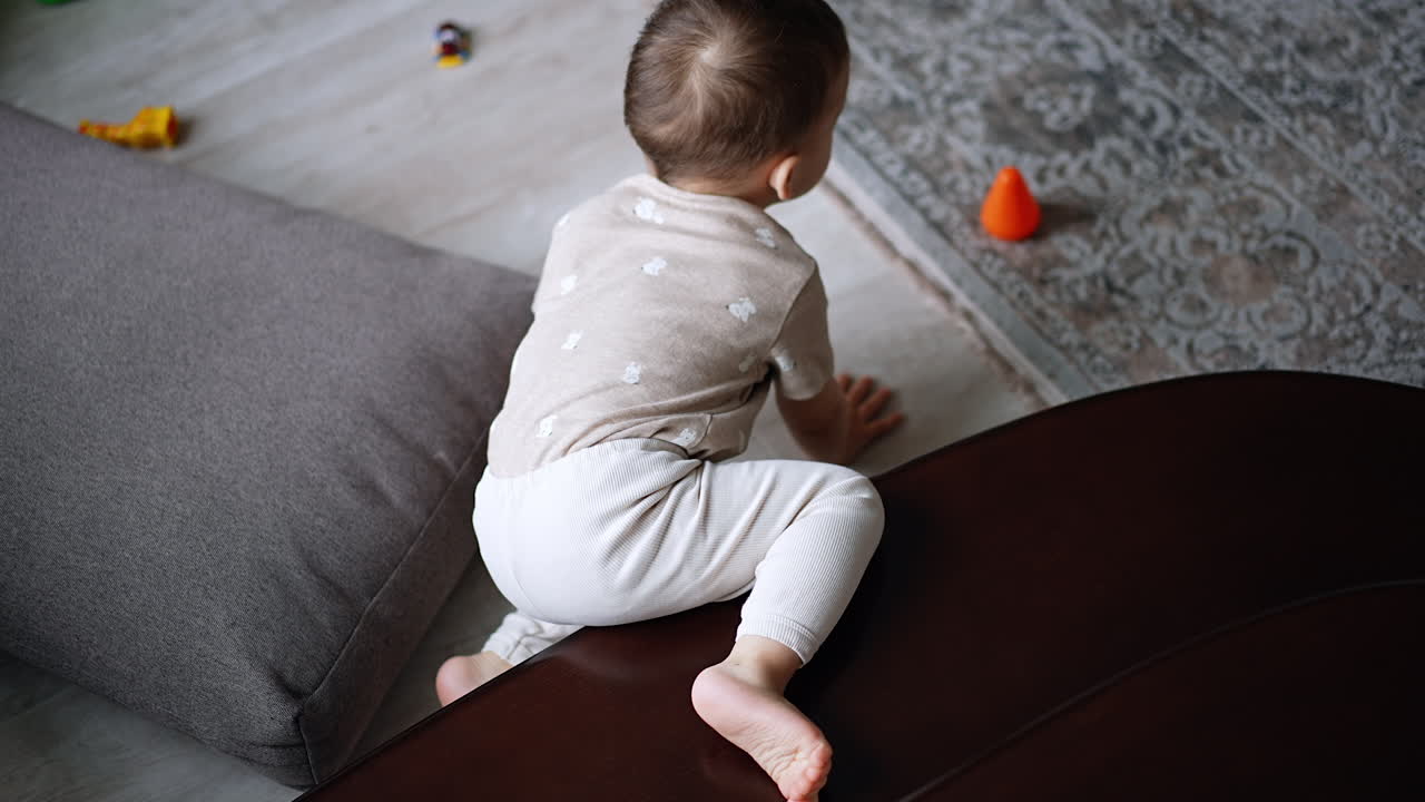Toddler boy crawls by the stairs in the room. Kid gets off the step and sits down on the floor near the cushion. Top view.