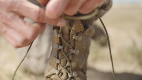 slow motion: a us marine positioned in the desert ties up his left boot as he prepares for battle