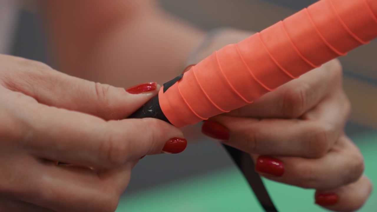 Closeup woman wrapping final overgrip, preparing badminton racket for tournament with meticulous tensioning and taping, steady hands and focused concentration on green court surface