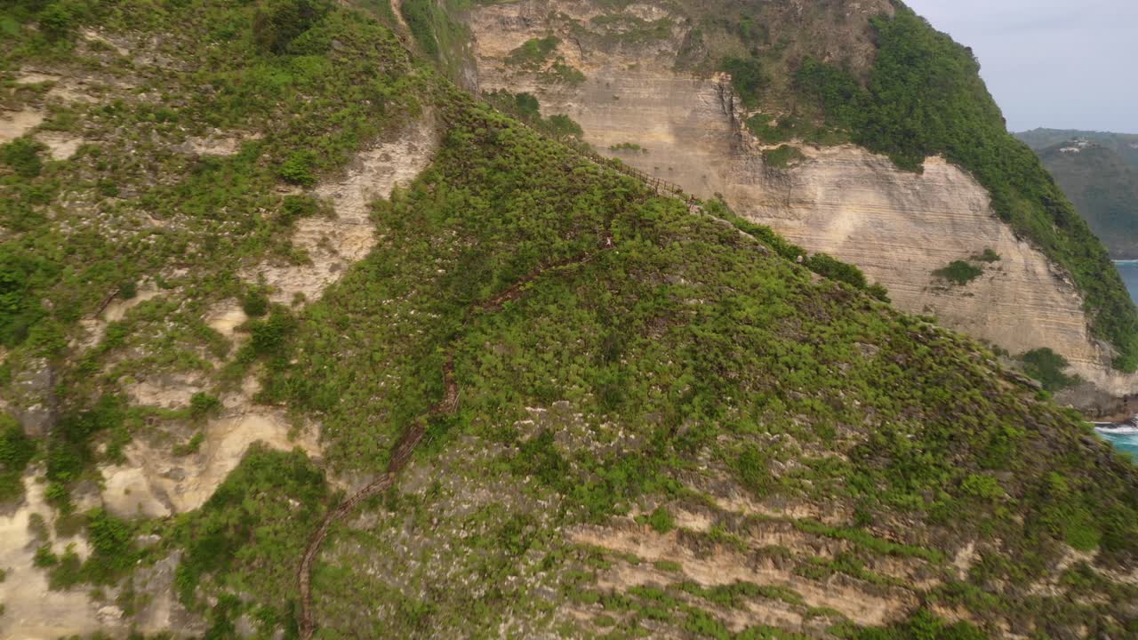 turista bajando las escaleras cubiertas de arbustos tropicales, tiro aéreo que revela la hermosa playa aislada de arena de kelingking y acantilados en la isla de nusa penida, bali