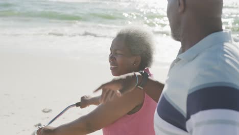 happy senior african american couple walking with bikes at beach, in slow motion