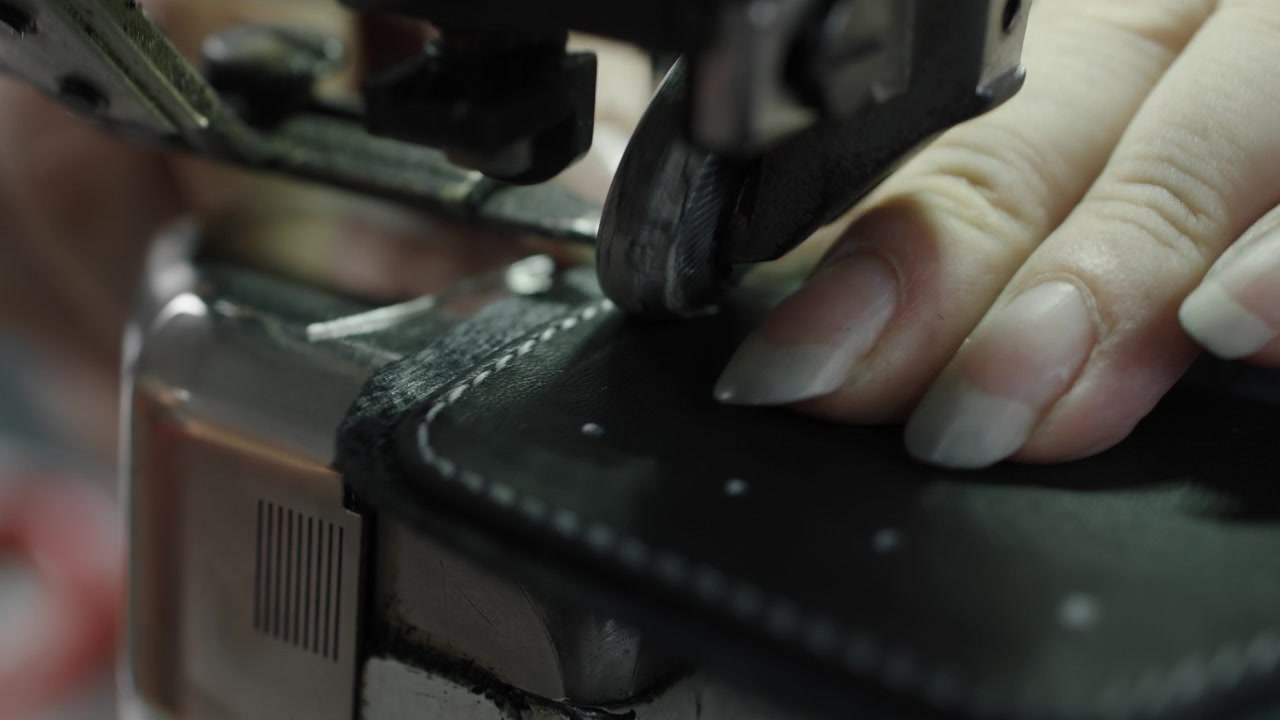Close up of hands sewing leather shoe material with industrial sewing machine