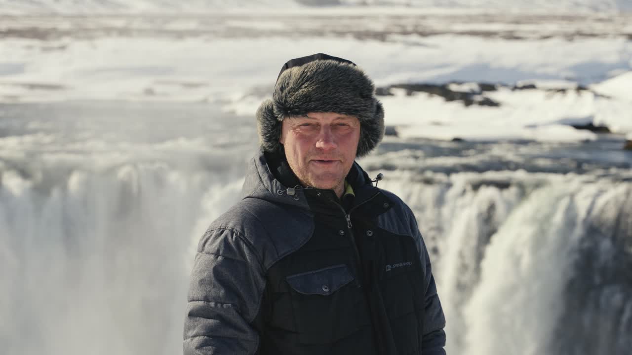 카메라를 바라보는 남자, 배경에는 거대한 고다포스 폭포, 아이슬란드