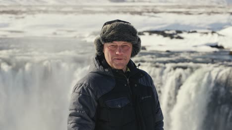 man look into camera, massive godafoss waterfall in background, iceland