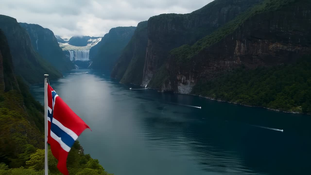 Vlající norská vlajka na kovové tyči se vlní ve větru, dron se oddaluje a odhaluje fjord