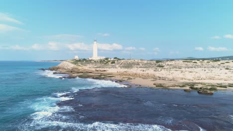 Aerial-view-from-a-drone-of-a-lighthouse-by-the-sea-and-the-beach-on-a-sunny-day