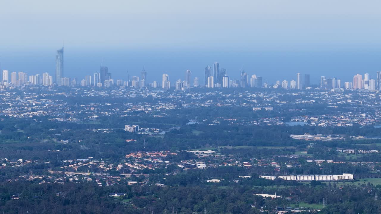 Wide aerial pan reveals Gold Coast highrises, suburban sprawl, and lush hinterland under daylight