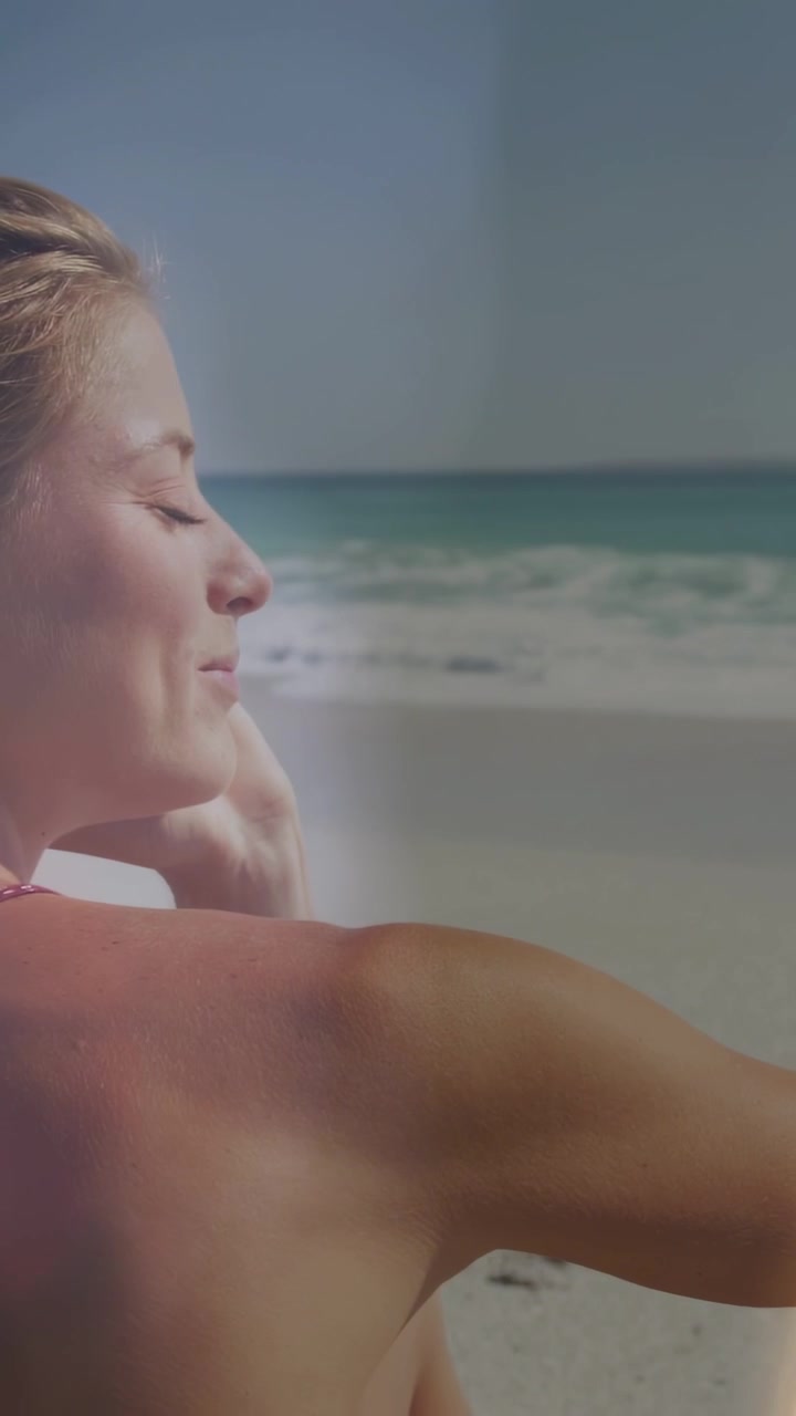 Video verticale: Donna in spiaggia, con la mano che le fa ombra agli occhi dal sole mentre il bokeh si muove sul viso, per il viaggio.