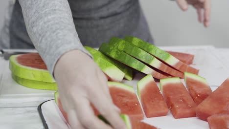 slicing red watermelon into small pieces on a white cutting board.