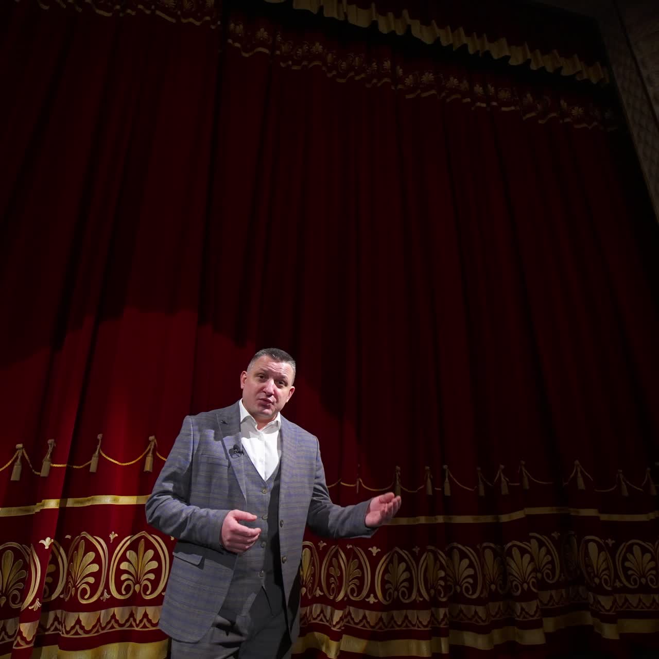 Actor with microphone announces performance before auditorium. Theater curtains background