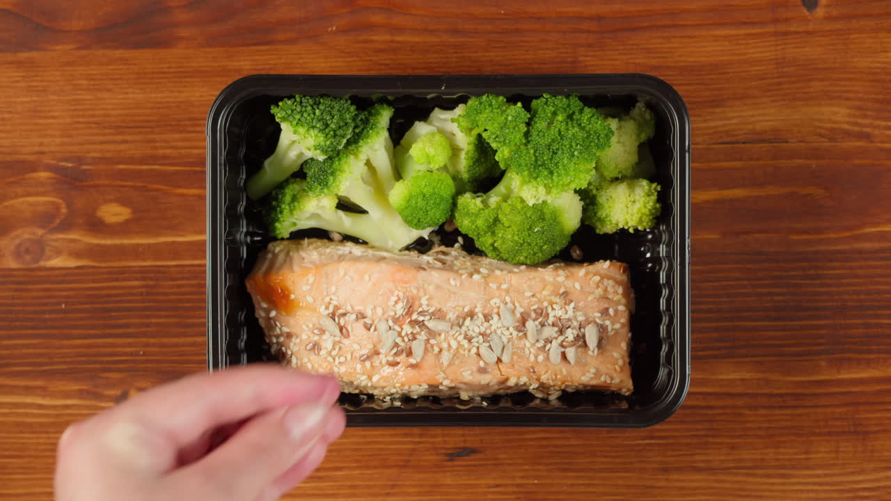 Hand Sprinkling Seeds on Salmon and Broccoli Meal Prep